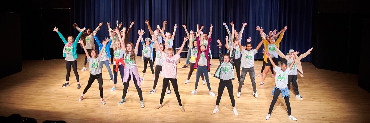 Photo of Theater Academy students with their arms raised, performing in a musical